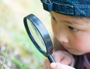 girl with magnifying glass looking at flower